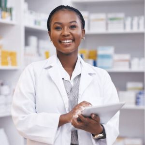 Portrait of black woman in pharmacy with tablet, smile and online inventory list for medicine on shelf. Happy female pharmacist, digital checklist and medical professional checking stock in store.